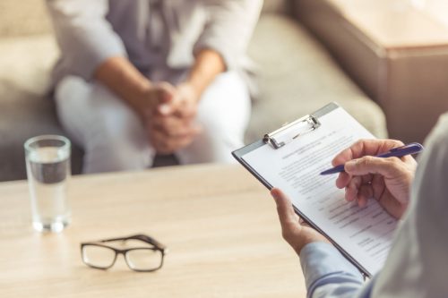 Cropped image of depressed man at the psychotherapist. Doctor is making notes while listening to his patient